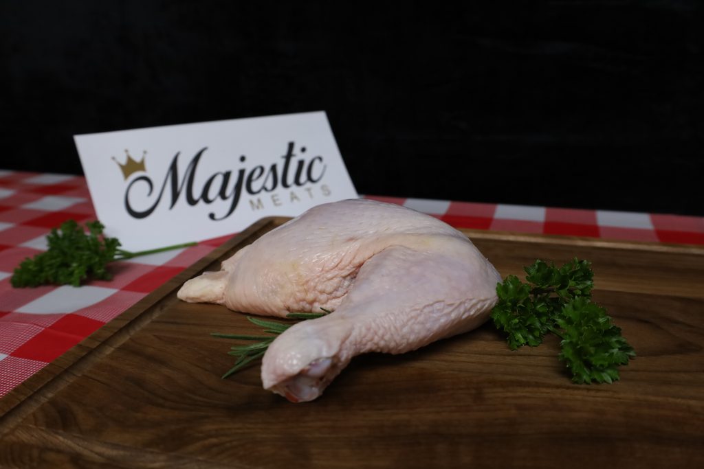 Majestic Meats chicken thigh on wooden board with parsley and rosemary garnish.