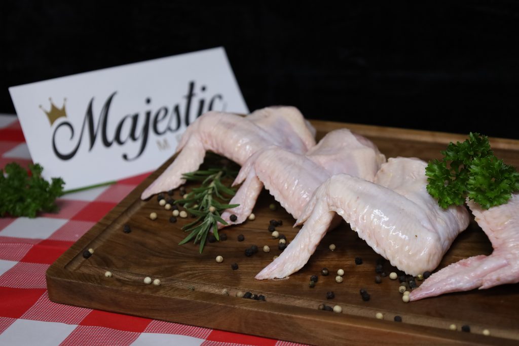 Majestic Meats chicken wings on wooden board with rosemary, parsley, and peppercorns.