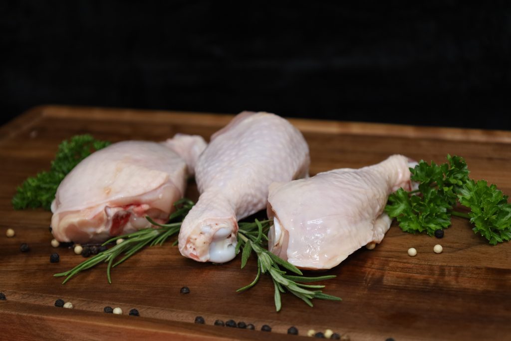 Chicken drumsticks on wooden board with rosemary, parsley, and peppercorns.