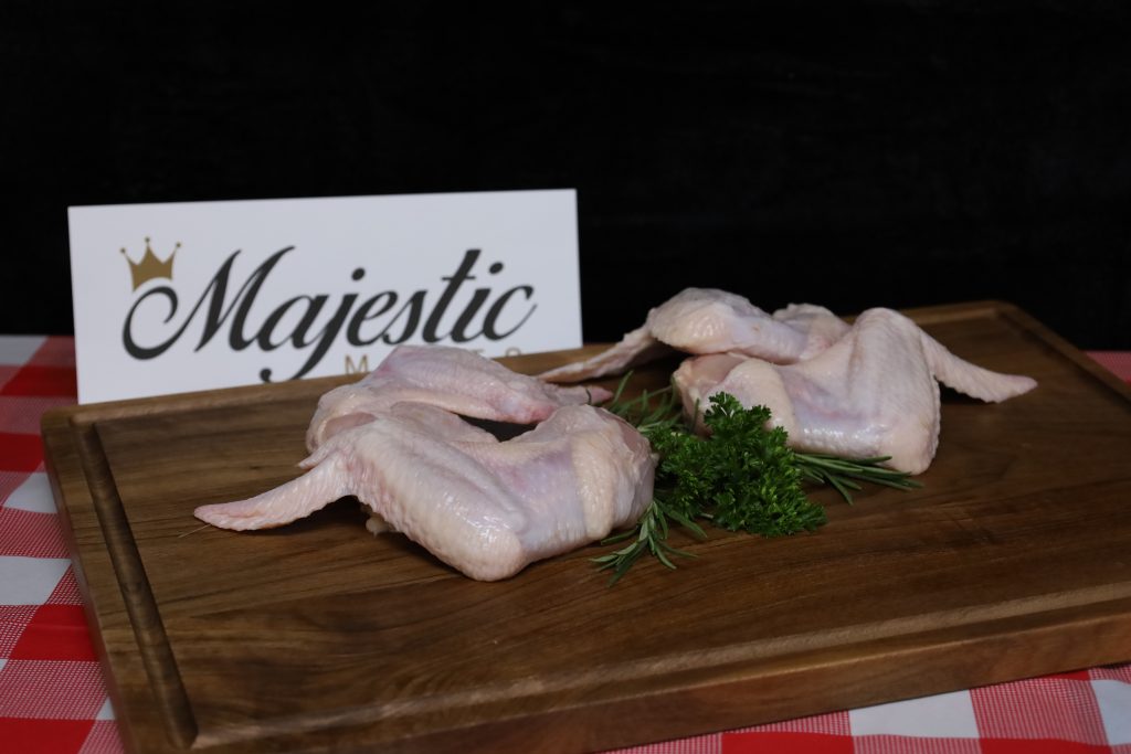Majestic Meats chicken wings with parsley on wooden board, brand sign visible.